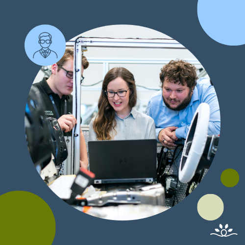 Three people, two men and one woman, collaborating around a laptop in a lab setting. The woman in the center wears glasses and smiles while typing, with lab equipment and wiring around them. The image is circular over a dark blue background with green, cream, and blue accent circles. Upper left features a white faculty icon in a blue circle. NDCSS logo bottom right.