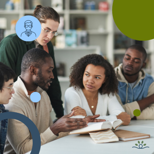 Group of five diverse students gathered around a table in a library, deeply engaged in discussion. A man in a gray sweater gestures toward an open book, while others listen attentively. Shelves of books form the background. Circular overlays in light blue and green appear around the edges. Upper left contains a white faculty icon in a blue circle. NDCSS logo bottom right.
