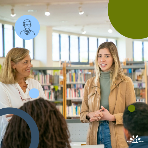 A woman in a tan jacket and green turtleneck speaks to a small group in a library, with shelves of books in the background. A faculty member in a white blouse and red necklace stands nearby, smiling. The audience is partially visible in the foreground. Circular overlays in green and blue frame the image. Upper left contains a white faculty icon in a blue circle. NDCSS logo bottom right.