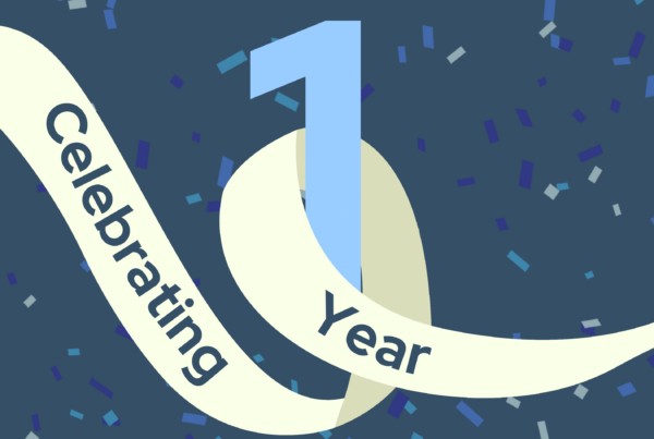 A celebration banner with a dark blue background covered in blue and white confetti. The center of the image features a large number "1" in light blue, wrapped by a cream-colored ribbon with the text "Celebrating 1 Year " in bold dark blue font.