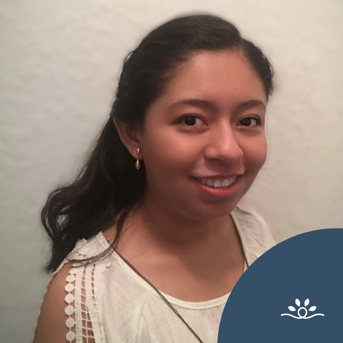 A head-and-shoulders portrait shows a young woman standing against a soft, light-colored background. She has long, dark hair pulled back, wears small gold drop earrings, and a sleeveless white top with delicate lace detailing along the shoulder. She smiles gently toward the camera. A curved dark blue graphic overlays the lower right corner, featuring the National Disability Center logo with a circular line and leaf motif.