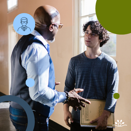 A classroom conversation scene shows two people standing near a large window with warm natural light. A Black middle-aged man wearing glasses, a light blue shirt, and a gray vest gestures with his hands while speaking. Facing him is a younger student with light skin and curly dark hair, wearing a gray long-sleeve shirt and holding a folder and notebook against his chest while listening. The layout includes several graphic elements layered over the photo, including circular shapes in blue and green, a small icon of a person inside a light blue circle, and a curved dark blue arc in the lower corner. The design uses rounded shapes and open space to frame the interaction and highlight the conversation between the instructor and student.