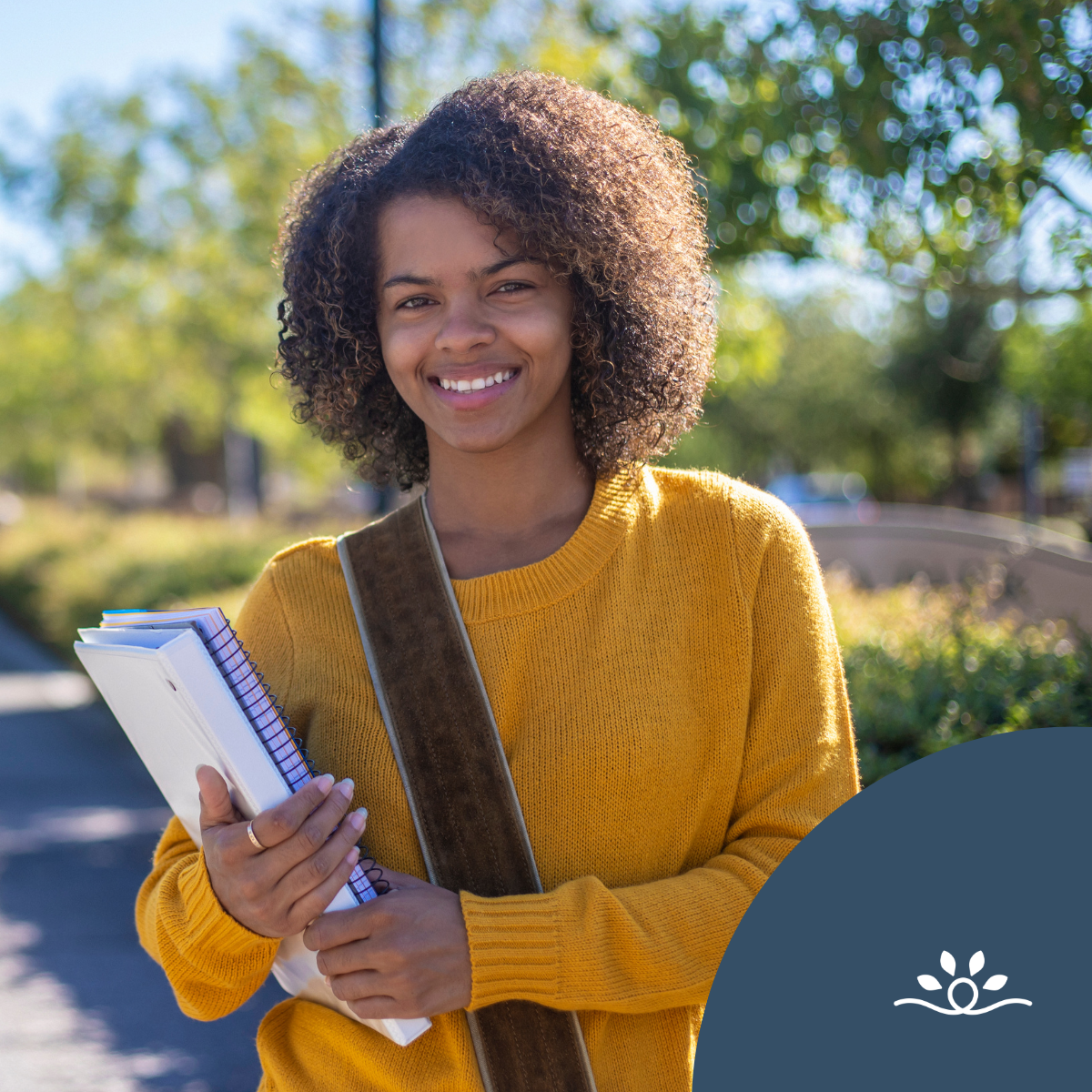 A college student stands outdoors on a campus walkway, smiling and holding notebooks. She wears a mustard yellow sweater and a shoulder bag, with trees and greenery in the background. The image represents student experiences in higher education, including decisions around disability disclosure and navigating access to support. A dark blue circular overlay with a white leaf-like logo appears in the bottom right corner.